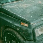 Close-up of a vintage green car with scratched paint and worn tires, showcasing an aged aesthetic.